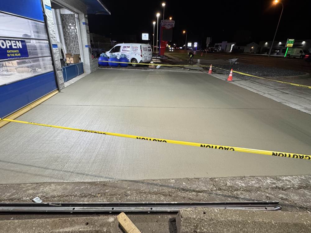 A new broom-finish concrete apron at a car wash, poured at night and taped off with caution tape