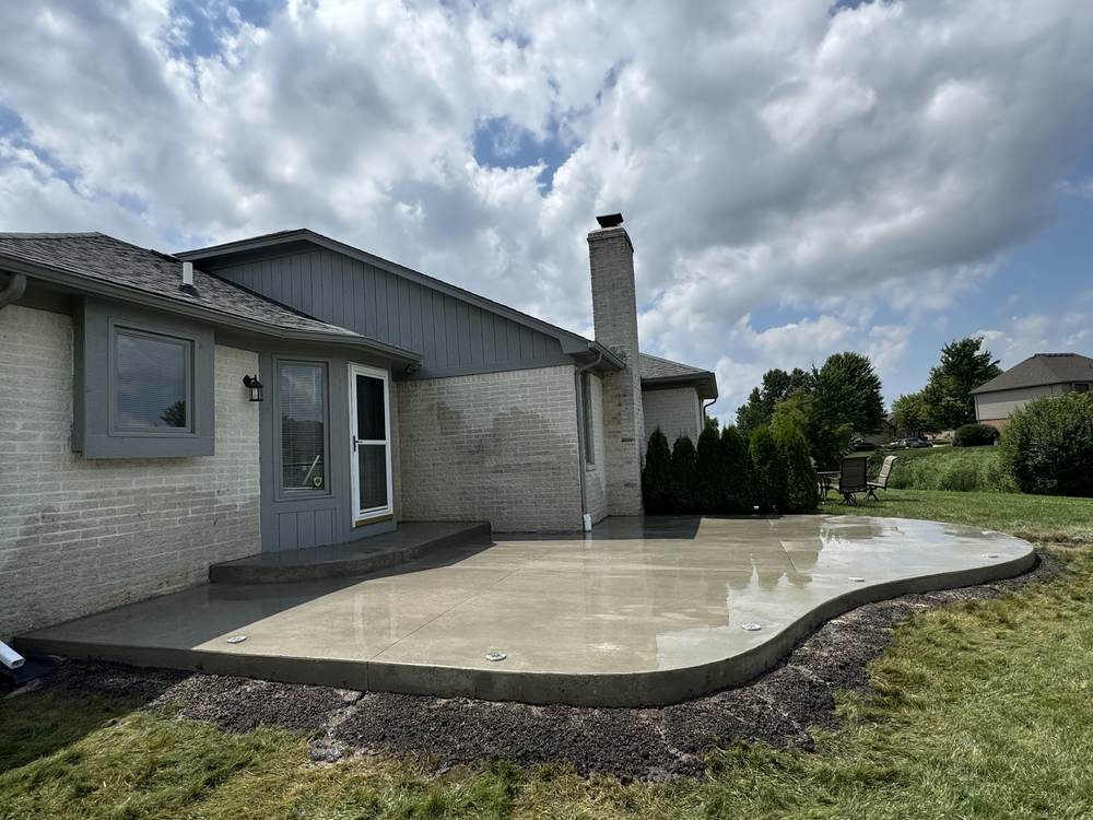 Freeform backyard concrete patio with a step-down landing, broom finish, just poured, behind a white brick house