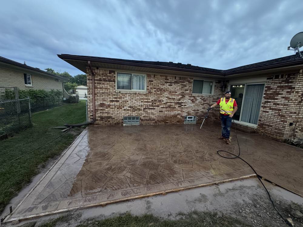 Stamped concrete patio in a random-stone pattern being washed down by a crew member in a safety vest