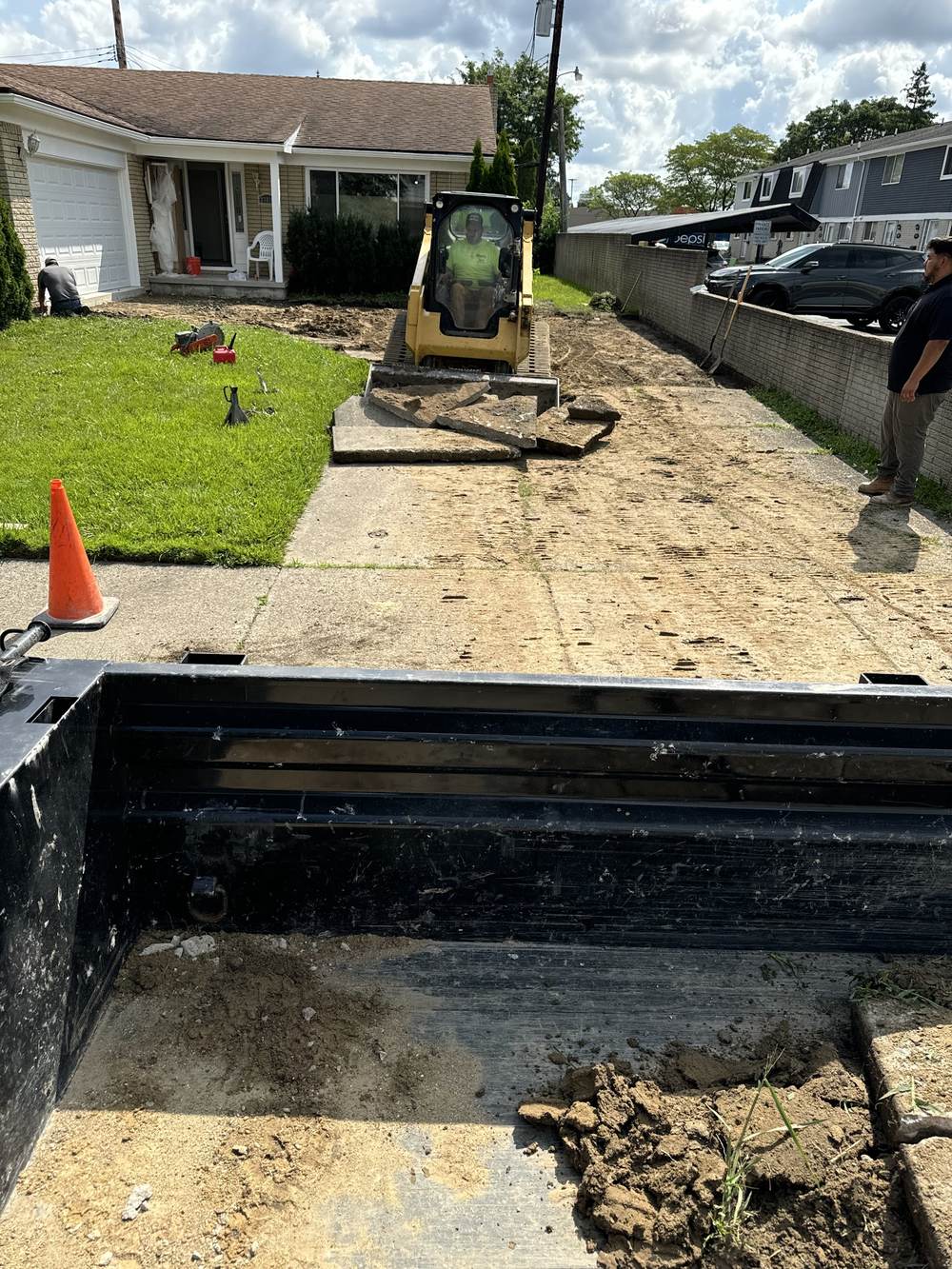 Crew member in a skid steer breaking up and lifting an old concrete driveway